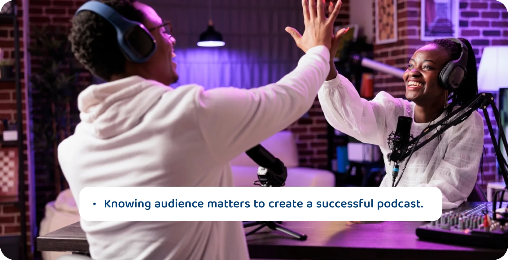 Podcast hosts high-fiving in a studio setup, signifying the joy of knowing their audience for podcast success.